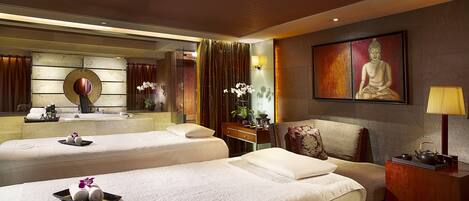 A hotel room with two beds, a sitting area, a large mirror, a Buddha painting, and a tea set on a side table.