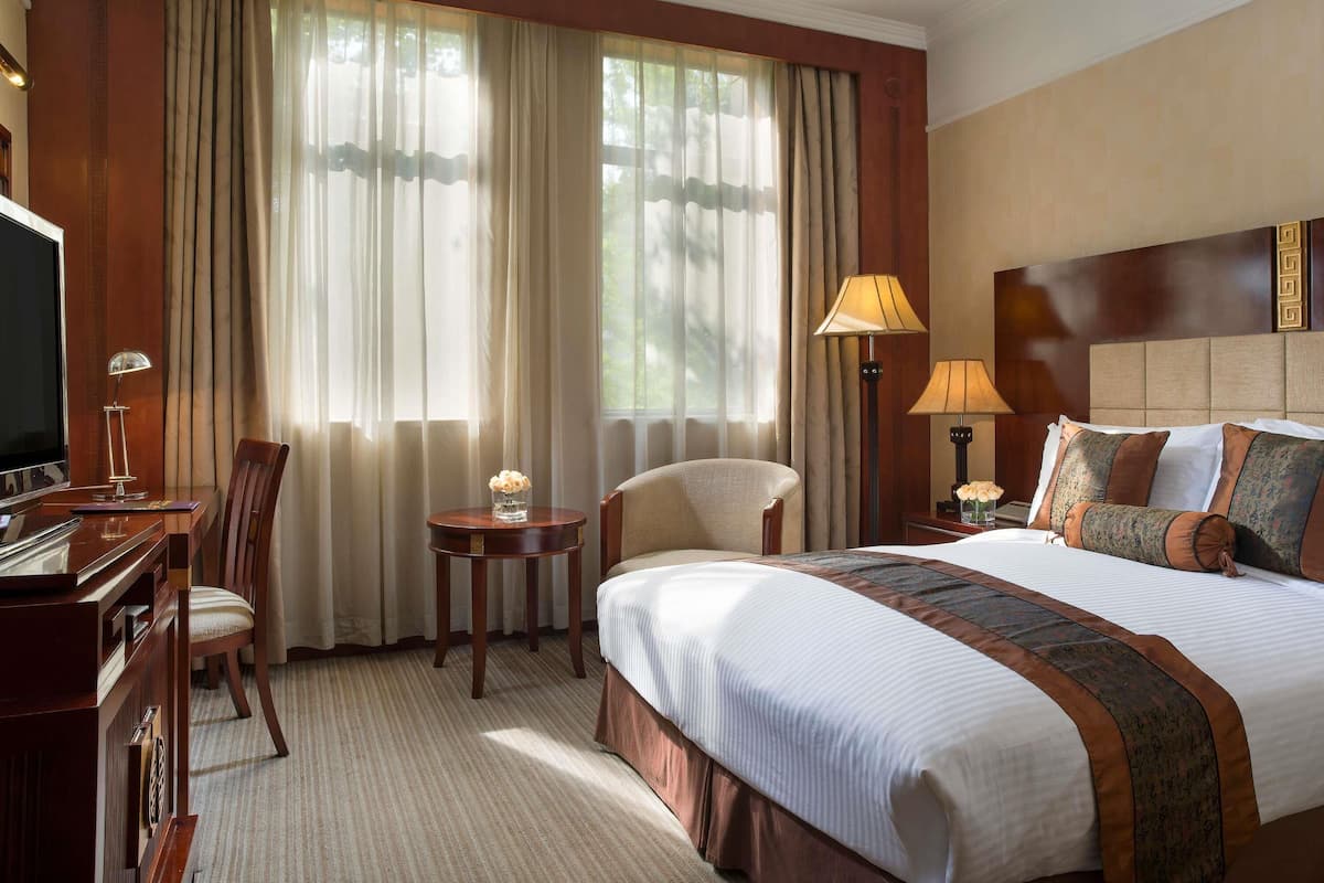 A hotel room with a large bed, a desk, a chair, a TV, and a window with curtains.