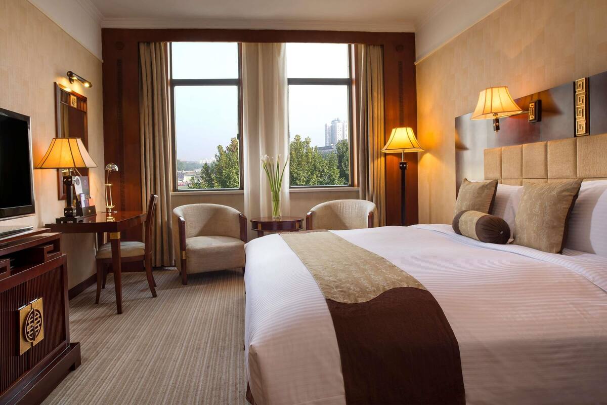 A hotel room with a large bed, two armchairs, a desk with a television, and two lamps.