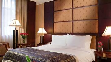 A hotel room with a large bed, two bedside tables, a nightstand, a lamp, and a vase with flowers.