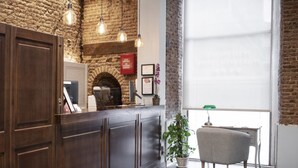 Un espace d’accueil avec un mur en pierre, un comptoir en bois, des luminaires suspendus, une plante en pot et une vue sur l’extérieur grâce à une grande fenêtre.