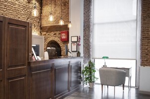 A reception area with a stone wall, wooden reception desk, hanging pendant lights, a potted plant, and a view of the outside through a large window.