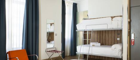 Habitación de hotel con literas, una cama individual, una silla, un espejo y una ventana con cortinas.