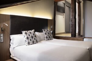 A neatly made bed with white linens and patterned pillows, a wooden headboard, and a large mirror reflecting the room's interior.