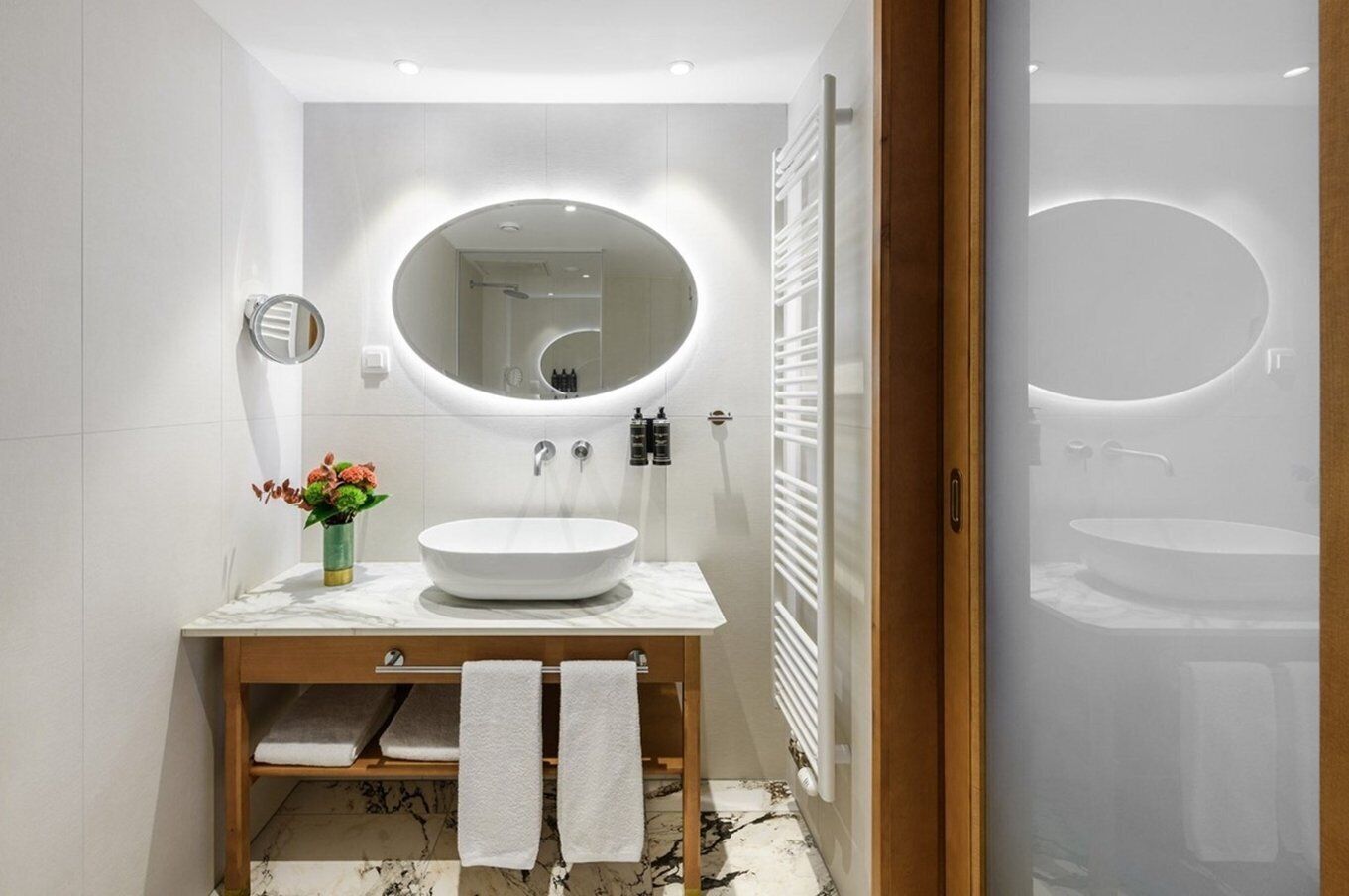 A modern bathroom with a round mirror, a white sink, and a towel rack.