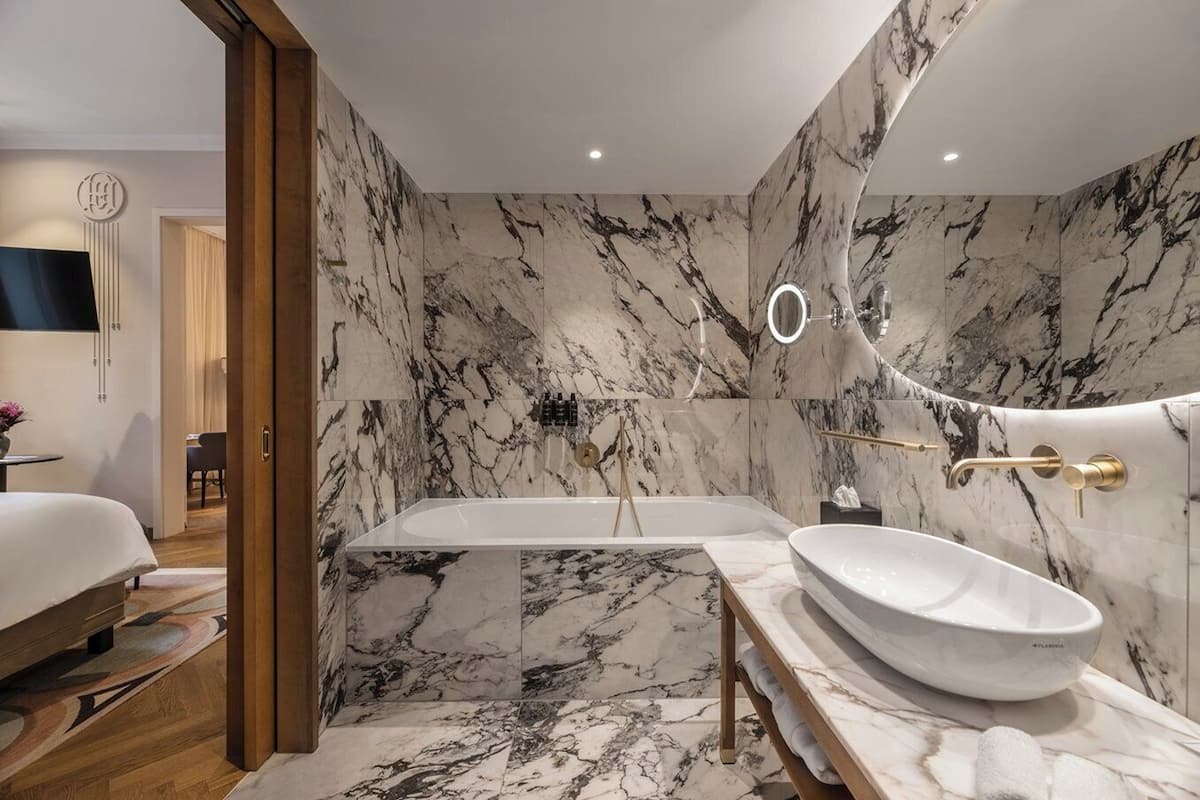 A modern bathroom with a marble wall, a freestanding bathtub, and a large sink.