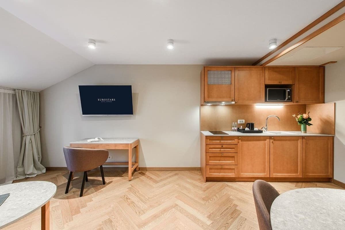 A compact kitchen with wooden cabinets, a microwave, and a sink. There is a small dining area with a table and chairs.