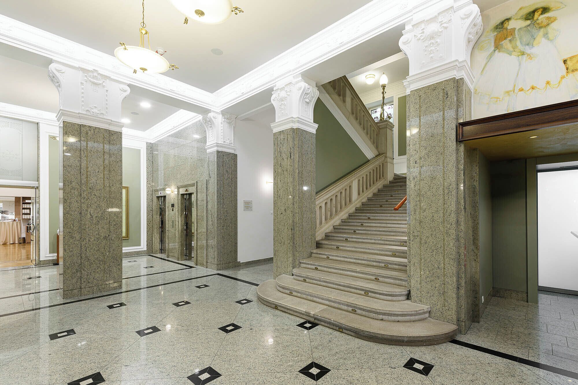 Un vestíbulo espacioso con suelo de mármol, una escalera central y columnas decoradas.