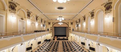 A large, ornate auditorium with tiered seating, a central stage, and elaborate wall decorations.