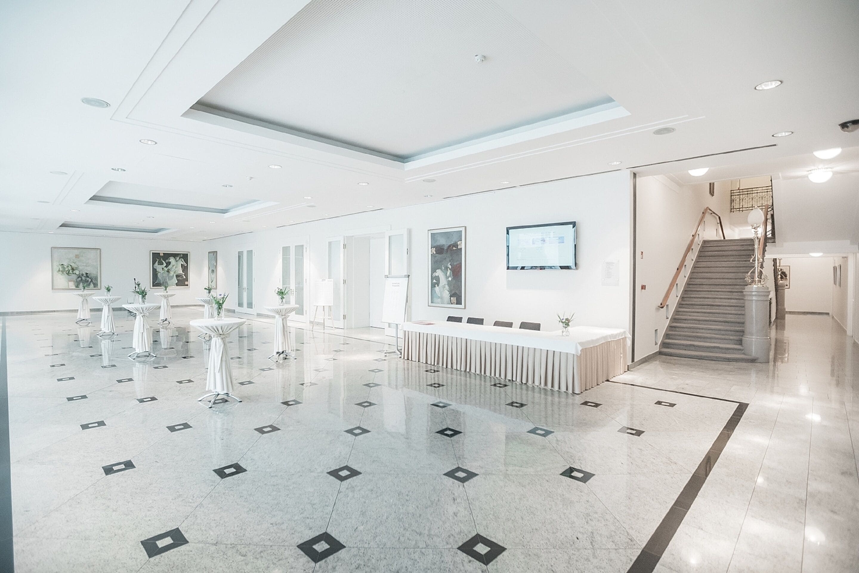 A spacious lobby with a polished marble floor, a reception desk, and a staircase leading to upper floors.
