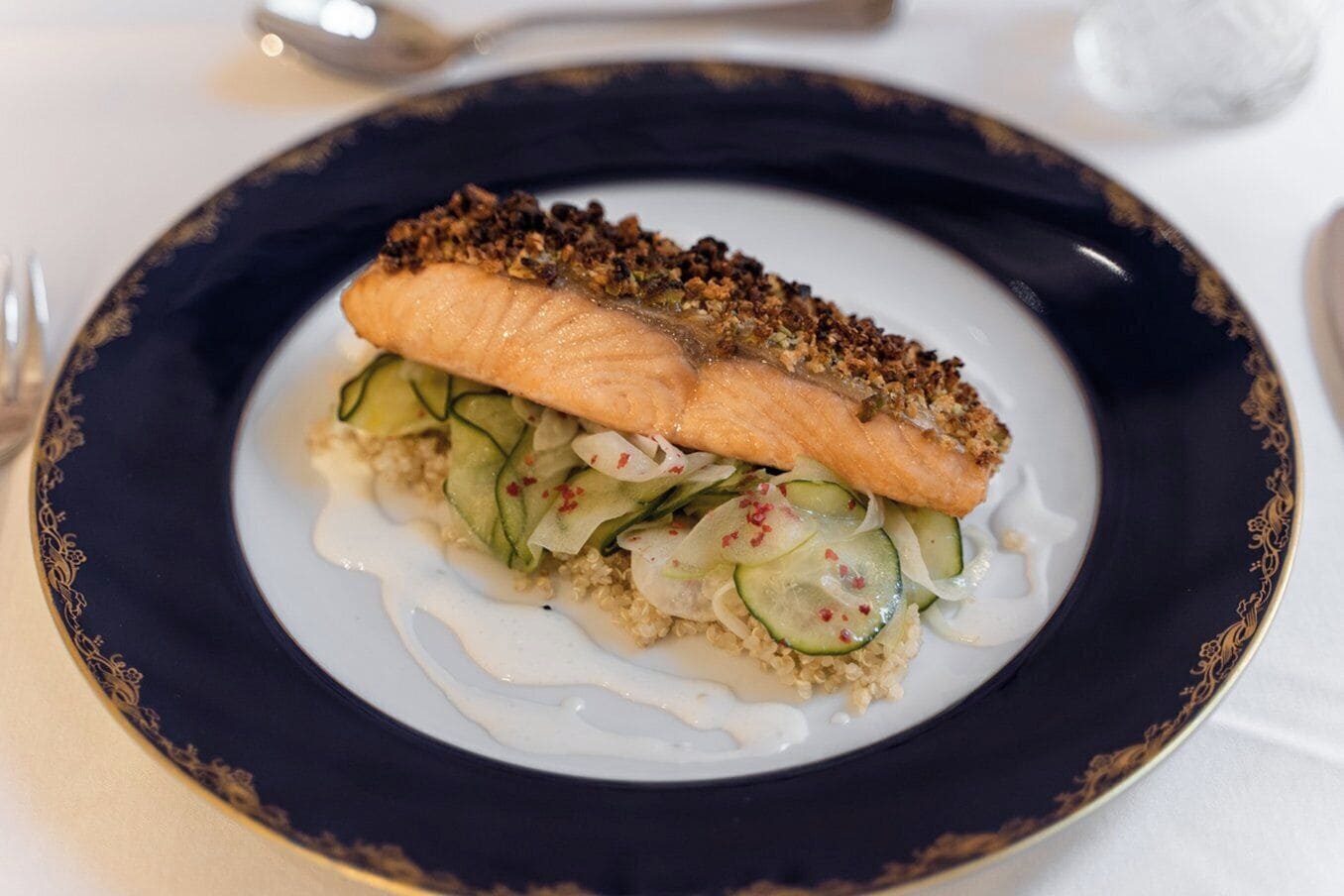 En tallrik med en bit lax, täckt med ett krispigt ströbröd, serverad med en gurksallad och en krämig sås.