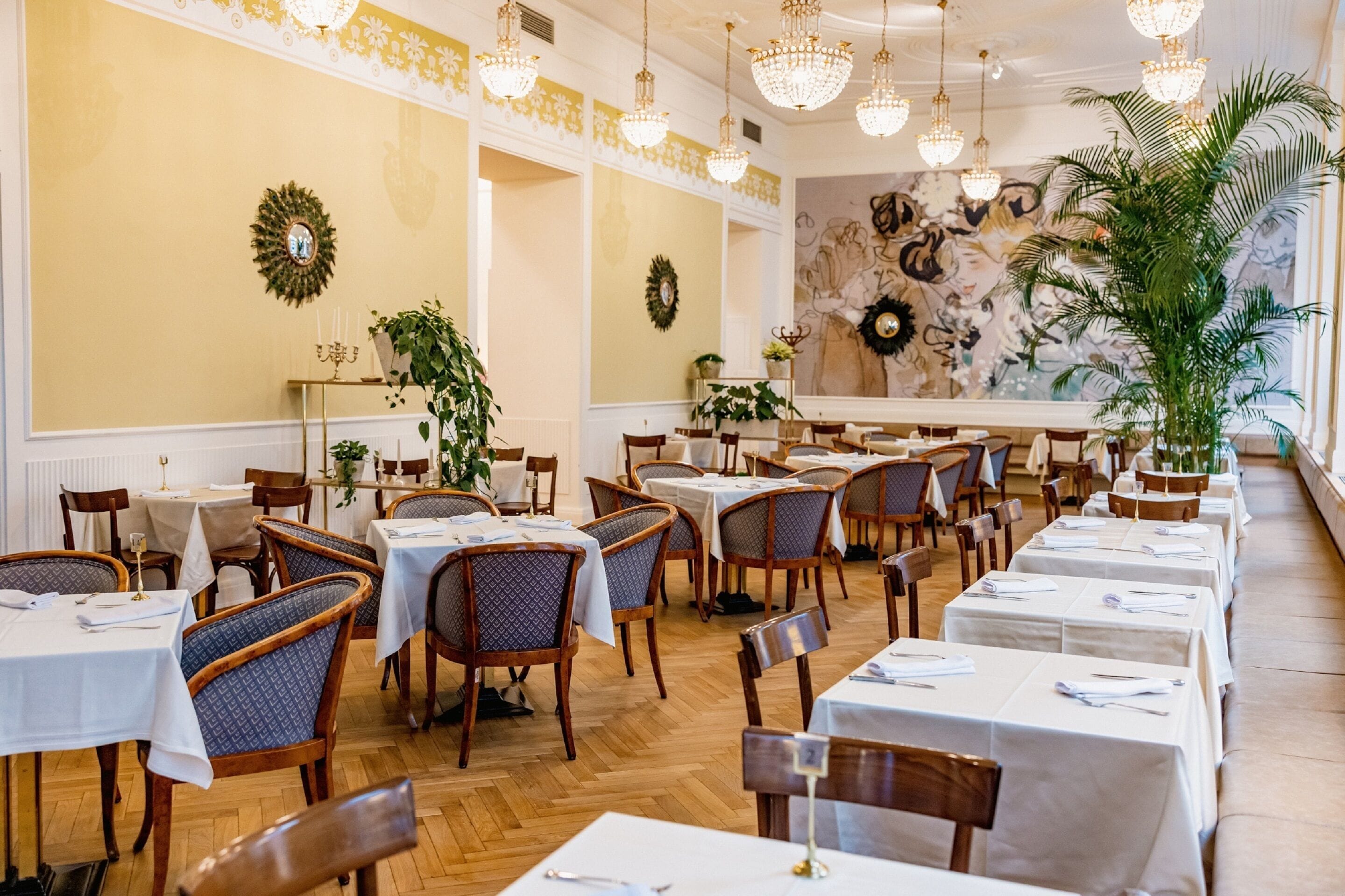 Un restaurante con varias mesas y sillas, candelabros y decoración mural.