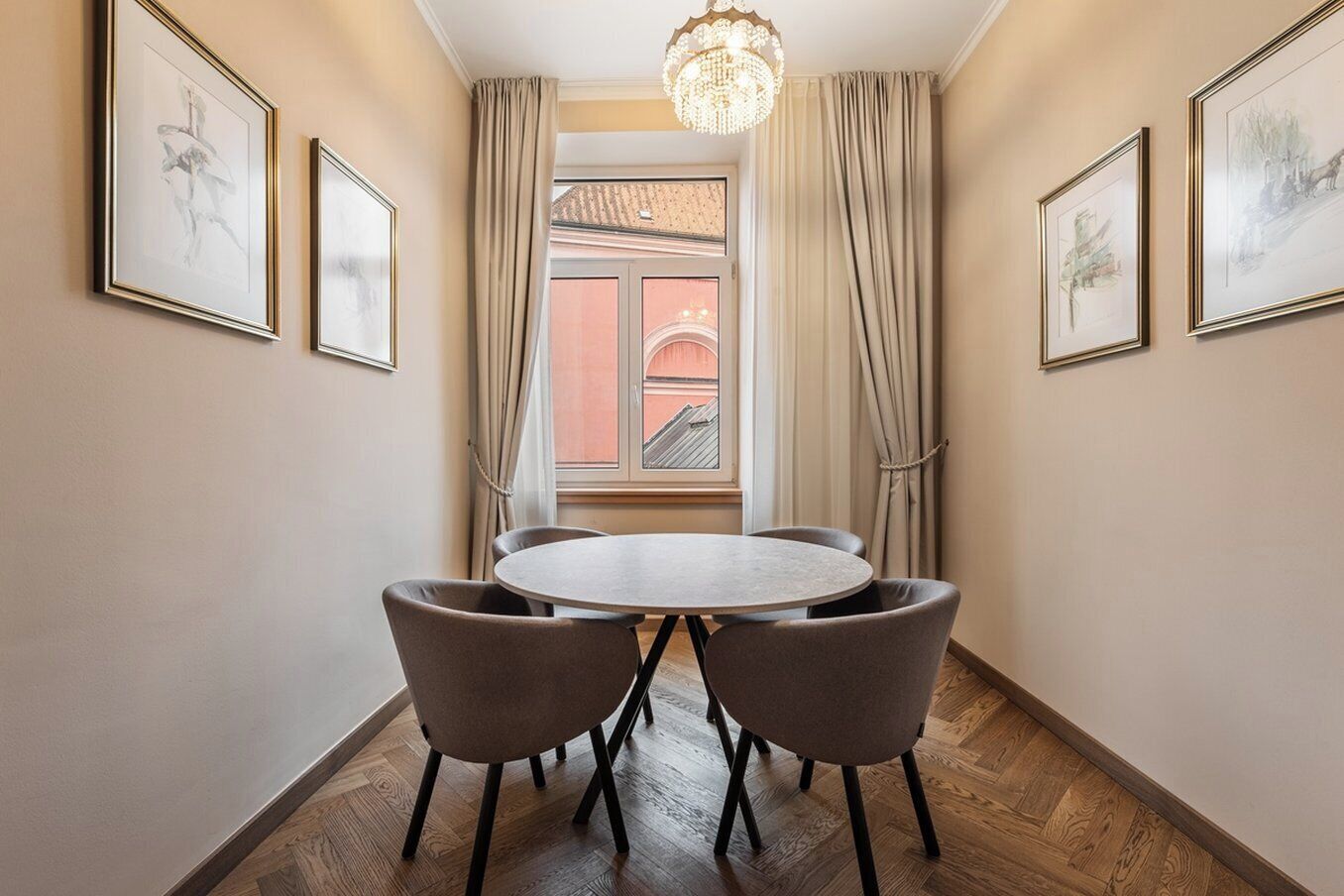 A hotel room with a round table and four chairs, a chandelier, and framed artwork on the walls.