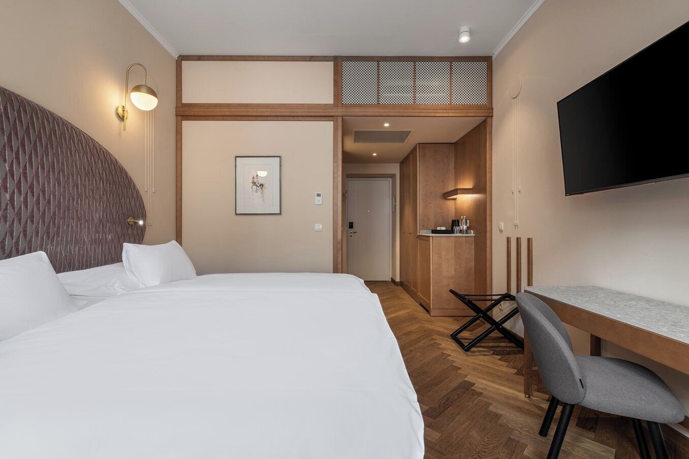 A modern hotel room with a large bed, a desk, and a TV.