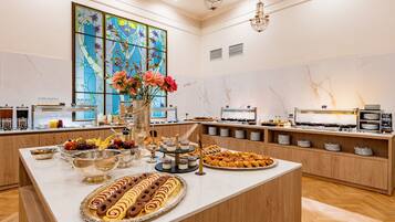 Um buffet com diversos alimentos, uma grande janela de vitrais e um lustre.