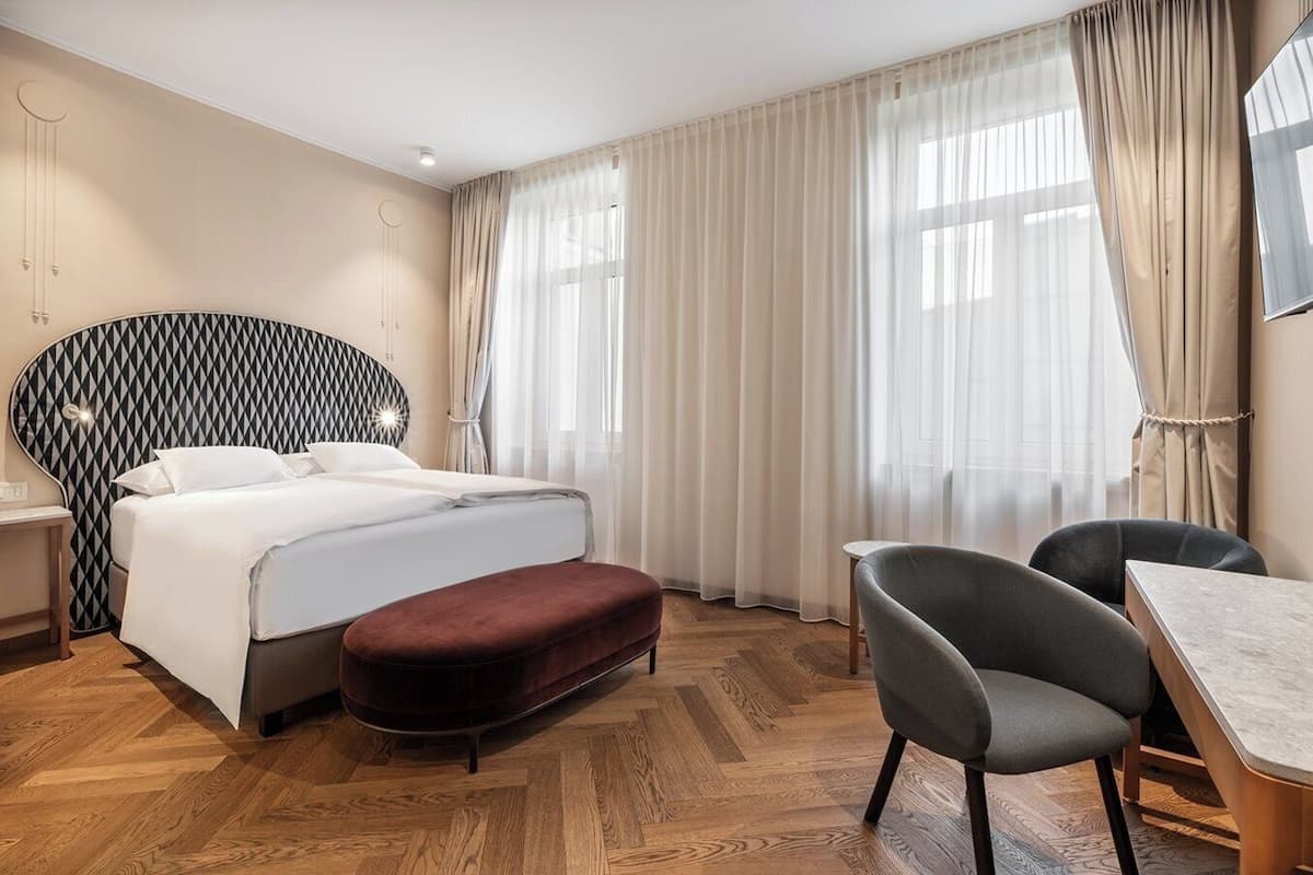 A hotel room with a bed, a desk, a chair, and a large window with curtains.