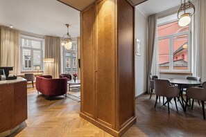 A modern hotel room with a wooden wardrobe, a dining area with a table and chairs, and a view of a building through the window.