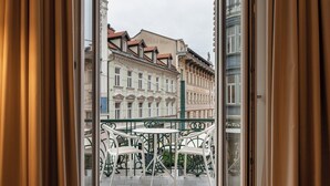 Varanda com cadeiras brancas e uma mesa, com vista para uma rua com edifícios históricos.