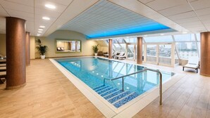 Piscina interna com vista clara da cidade através de grandes janelas, cercada por piso de madeira e elementos de design moderno.