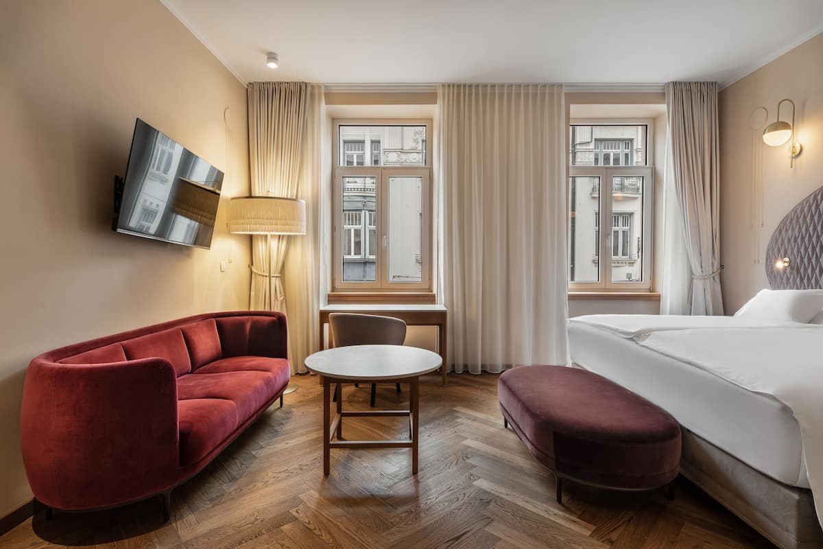 A hotel room with a red sofa, a round table, a bed, and a TV mounted on the wall.