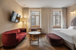 A hotel room with a red sofa, a round table, a bed, and a TV mounted on the wall.