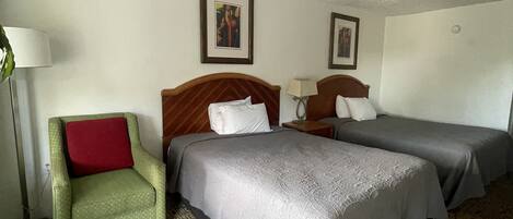 A hotel room with two single beds, a green armchair with a red cushion, and a patterned carpet.