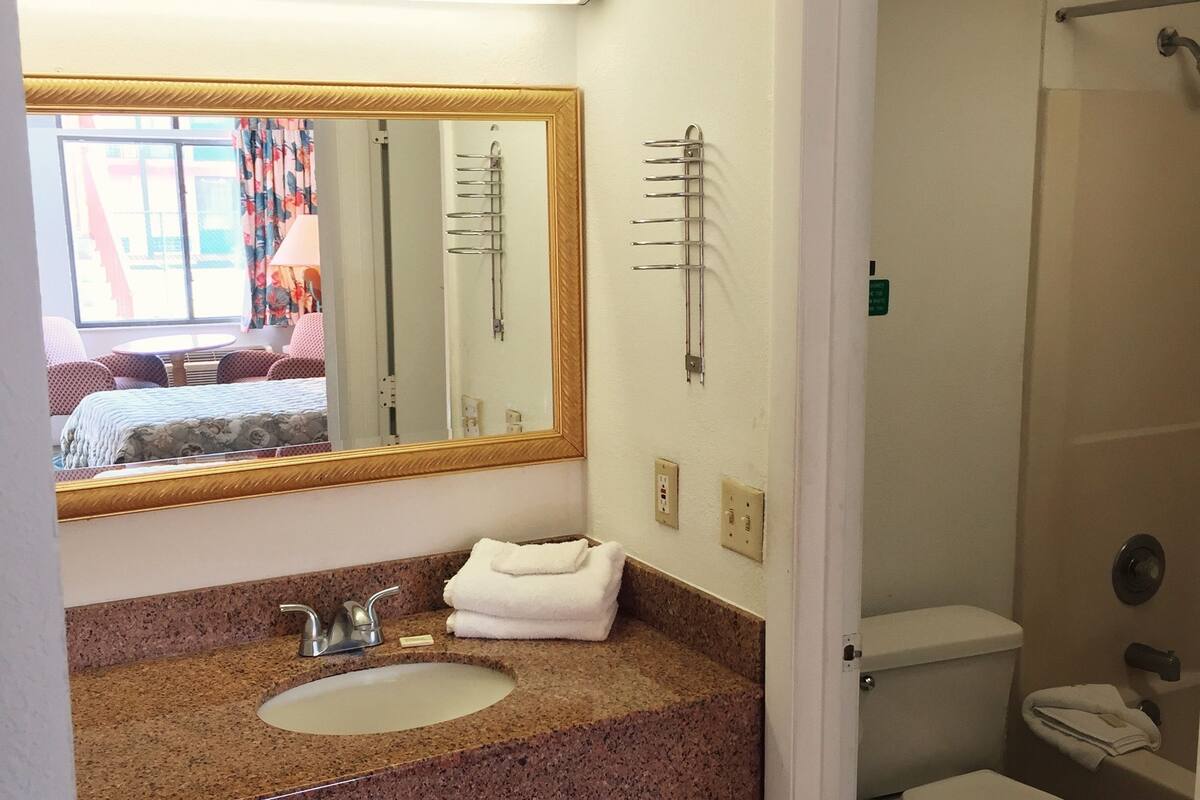 A bathroom with a granite countertop sink, a mirror, a towel, a toilet, and a shower area.