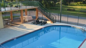 A rectangular swimming pool with a 4 FT depth marking, surrounded by a metal fence. There are lounge chairs and a covered seating area with tables. - Ambassador Inn (Kissimmee)