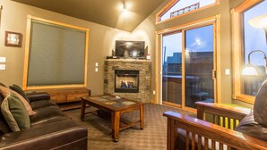 A cozy living room with a stone fireplace, a leather couch, a wooden coffee table, and a sliding glass door leading to an outdoor area. - Marys Lake Lodge Mountain Resort and Condos (Estes Park)