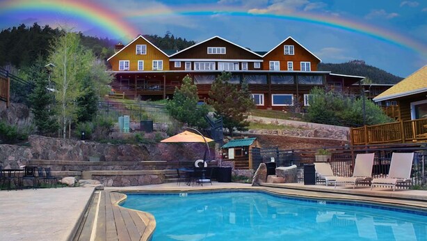 A wooden pool with lounge chairs, a covered patio, and a mountain backdrop. - Marys Lake Lodge Mountain Resort and Condos (Estes Park)
