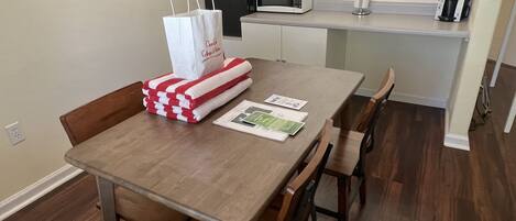 A small kitchen with a wooden table, chairs, a microwave, a coffee maker, and a white paper bag on the counter.