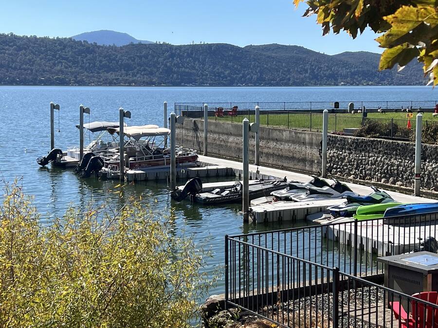 Un puerto deportivo con barcos amarrados, un muelle con zona de estar techada y vistas a un lago con colinas al fondo.