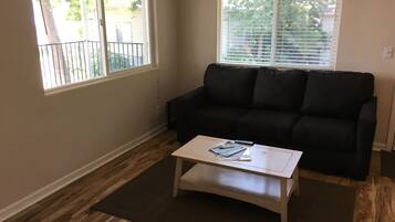 Un salon avec un canapé de couleur foncée, une table basse blanche et une fenêtre équipée de stores.