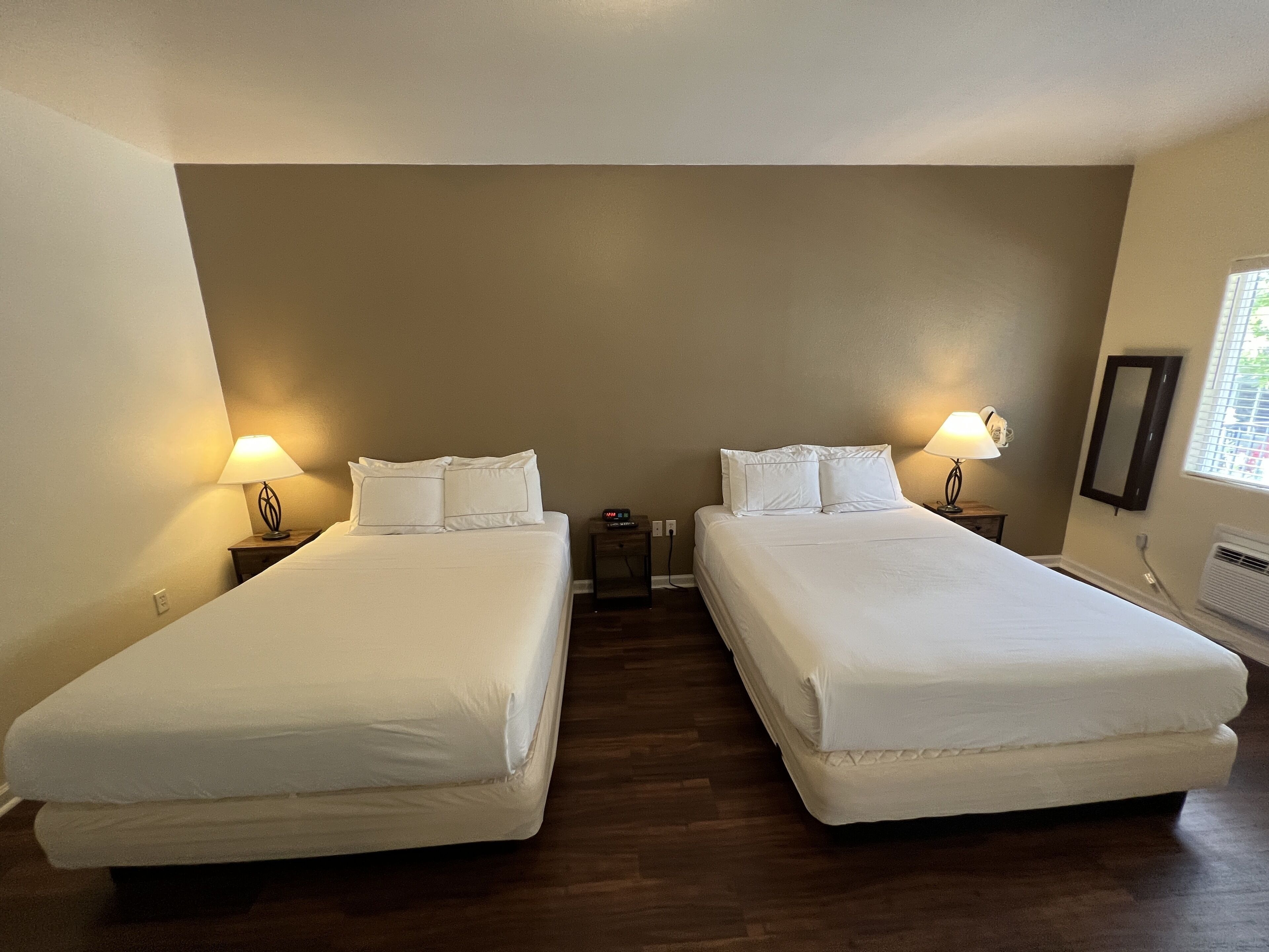 Ein Hotelzimmer mit zwei Betten, jeweils mit weißer Bettwäsche, einem Nachttisch mit Lampe und einem an der Wand befestigten Spiegel.