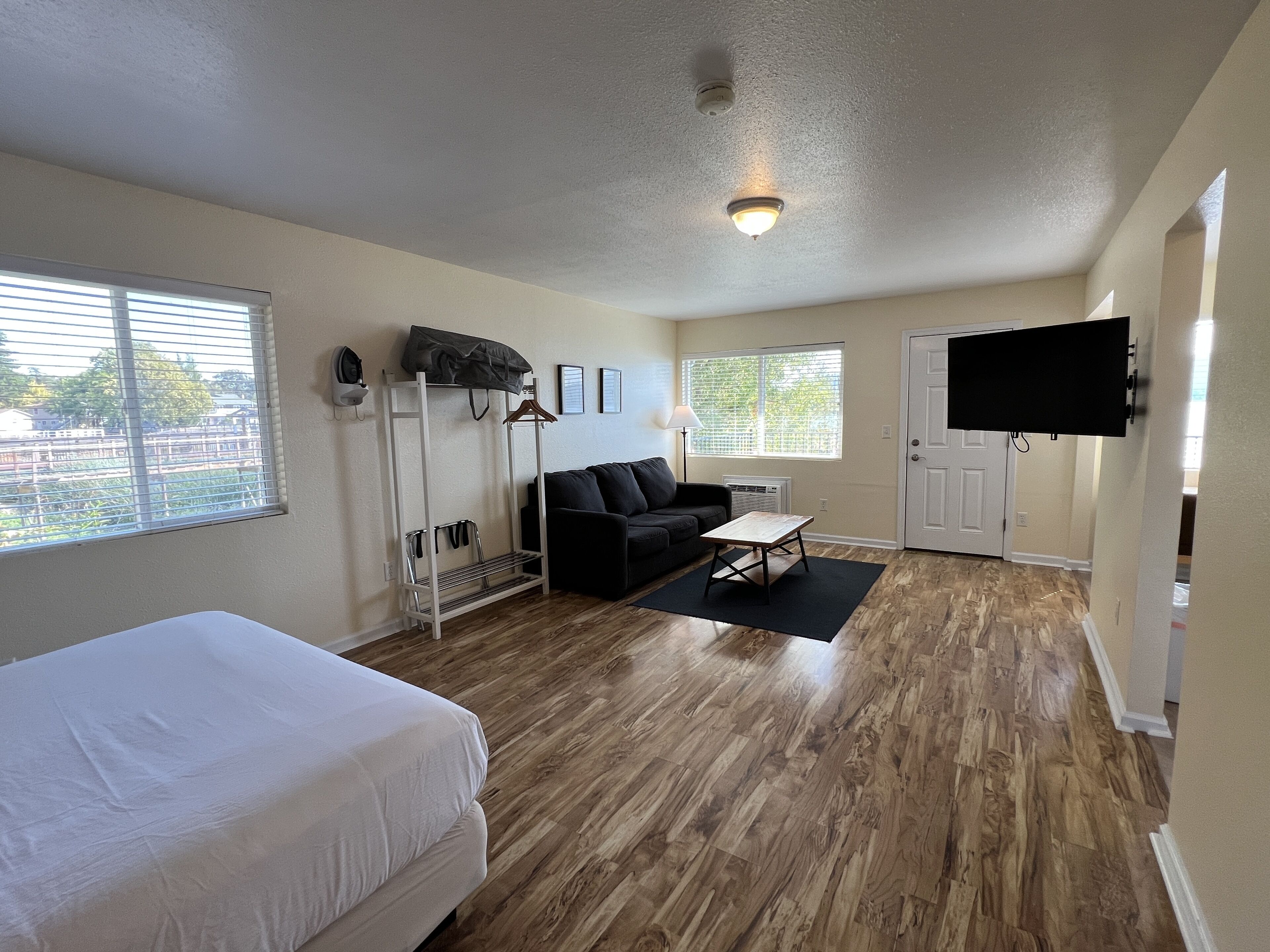 Una habitación con cama, sofá, mesa de centro, televisor y ventana con persianas.
