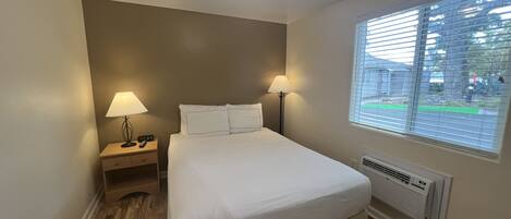 Un dormitorio con una cama, dos lámparas de noche, una mesita de noche, una ventana con persianas y una lámpara de techo.