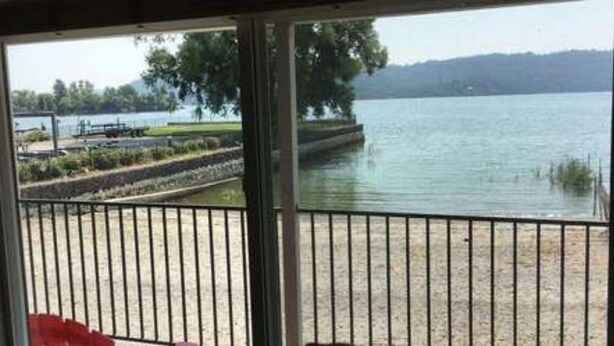 A view from a window overlooking a lake with a dock and greenery. - Clear Lake Cottages & Marina (Clearlake)