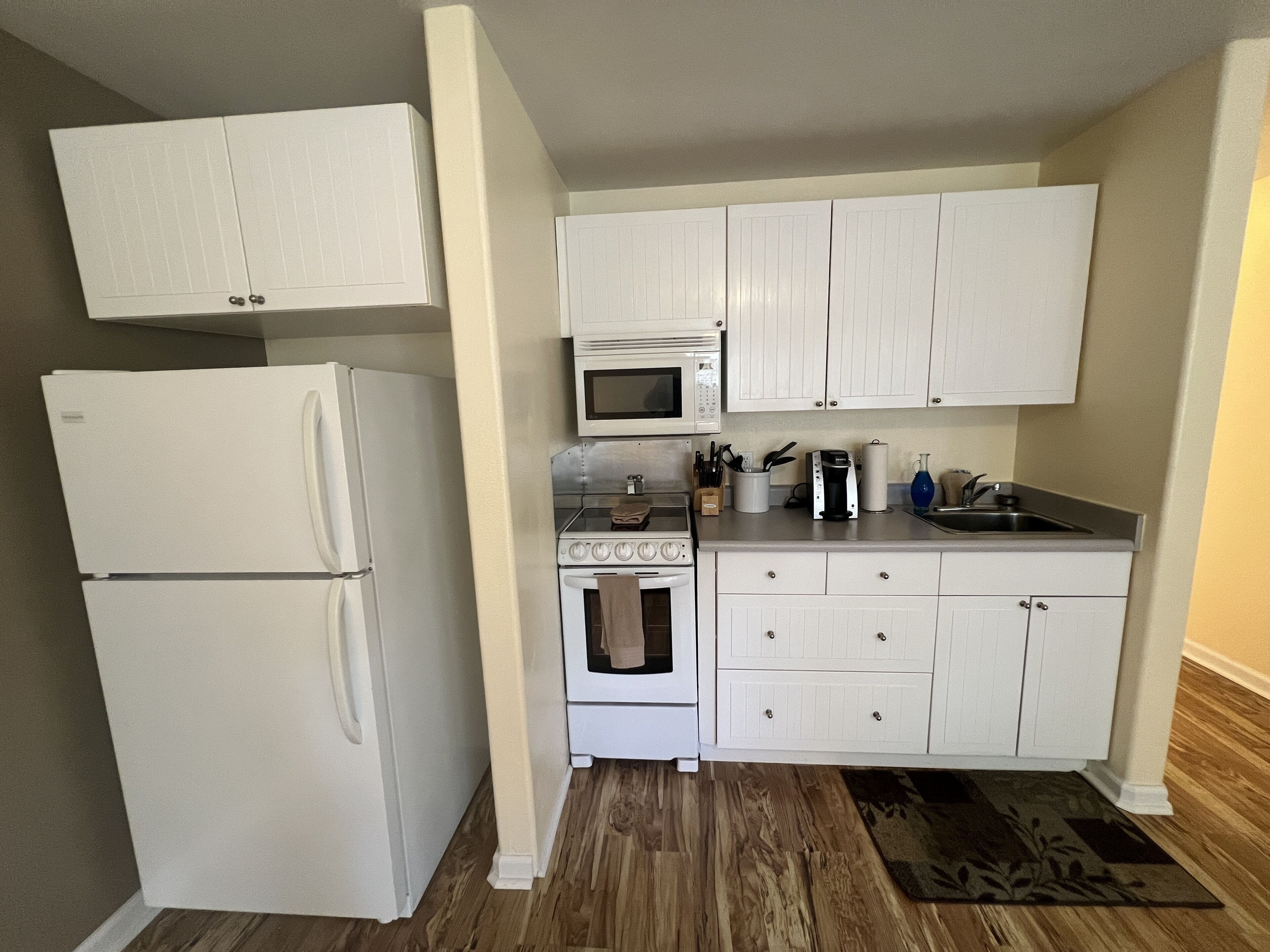 A compact kitchen with white cabinetry, a refrigerator, a microwave, an oven, and a sink.