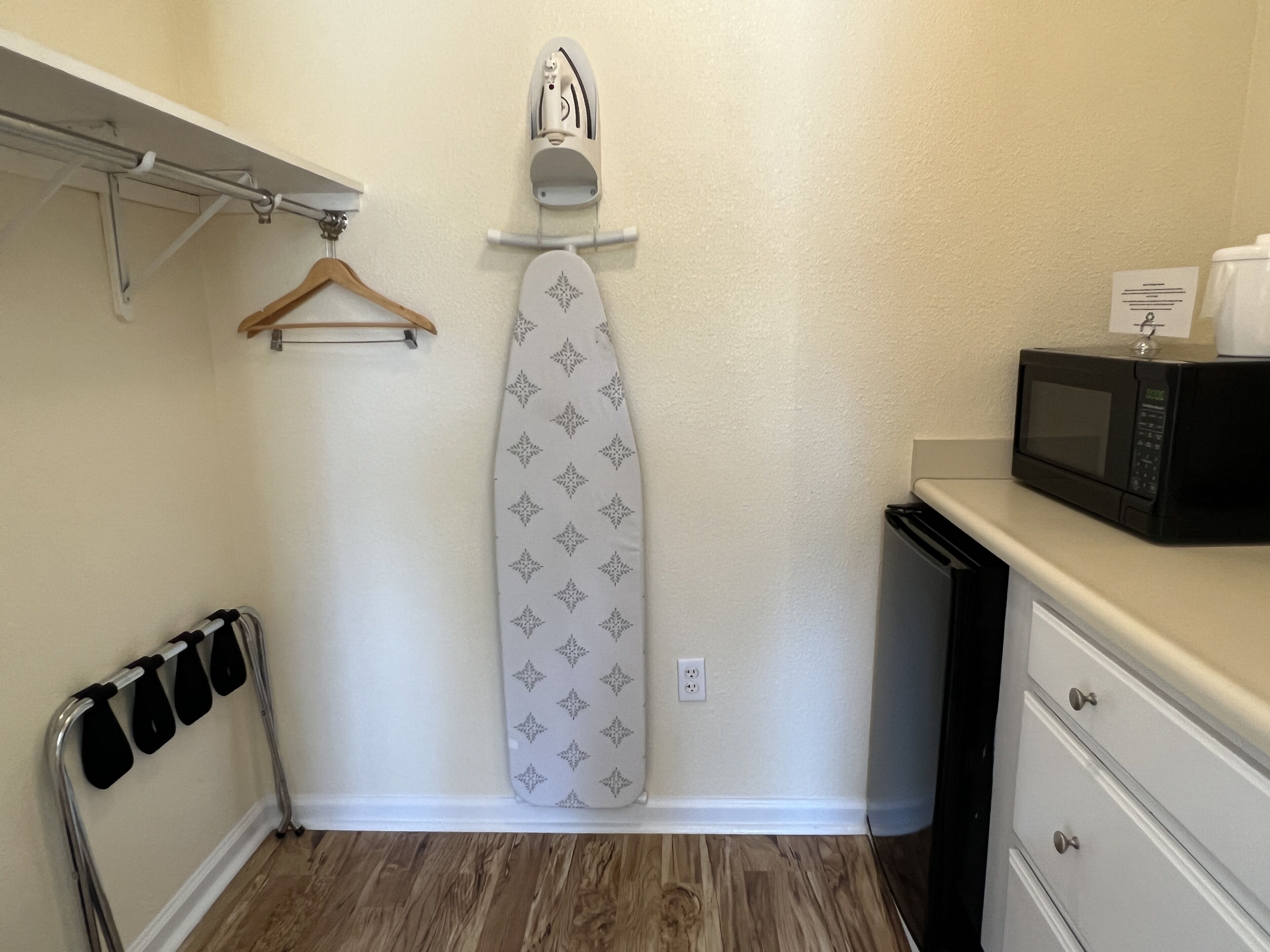 A compact kitchen with a microwave, ironing board, and a small cabinet.