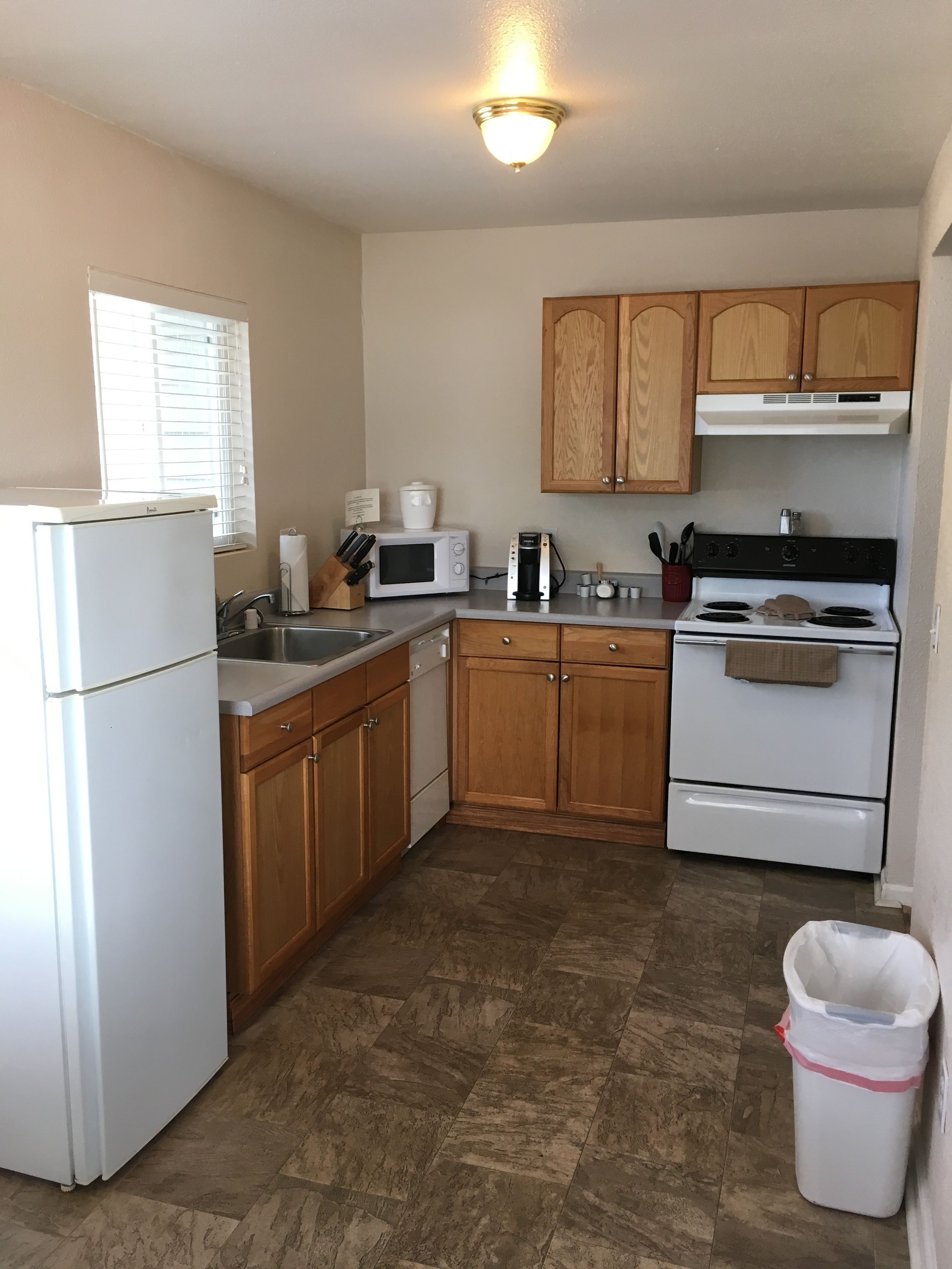 A compact kitchen with a refrigerator, microwave, stove, and wooden cabinets.