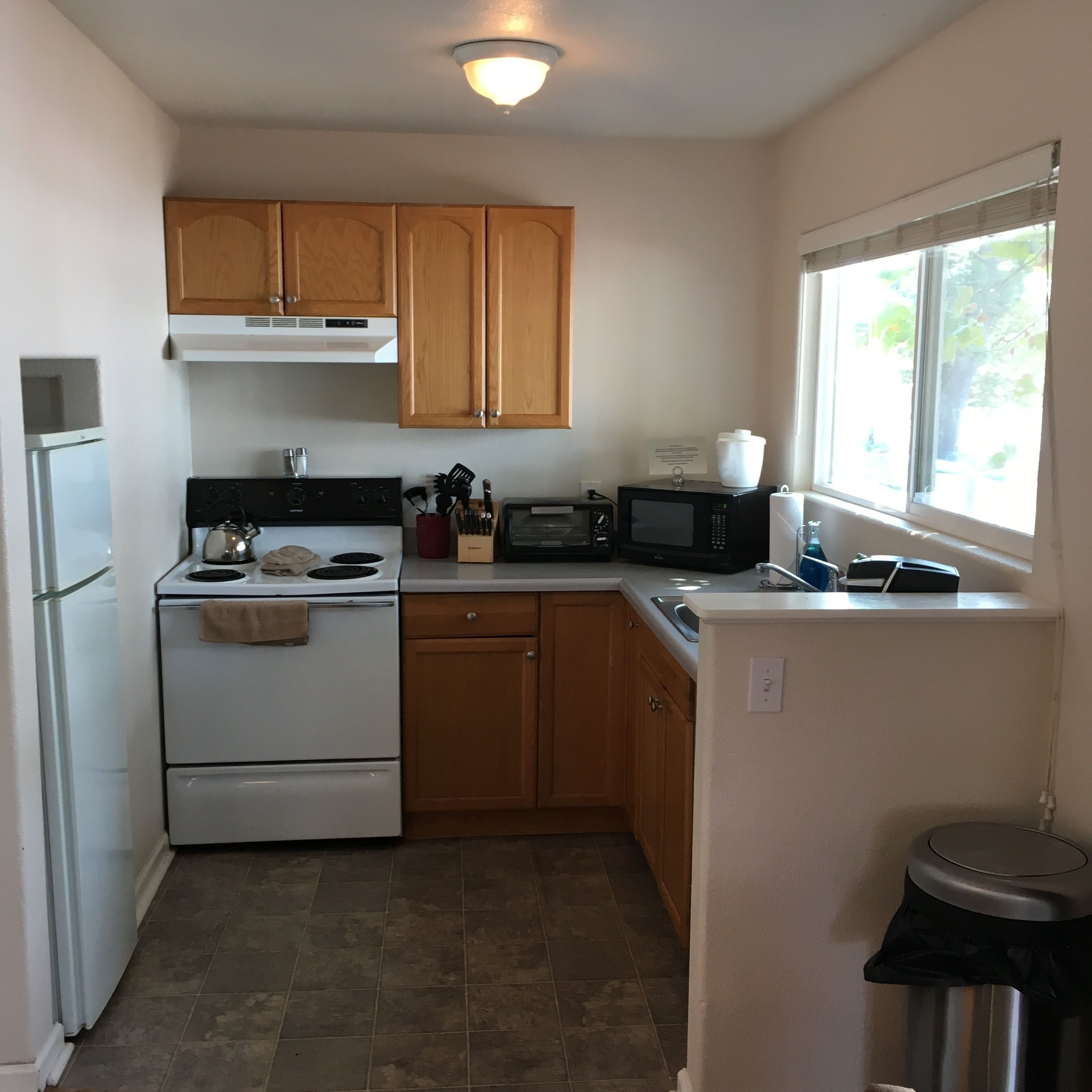 A compact kitchen with a stove, microwave, and sink. There is a window providing natural light.