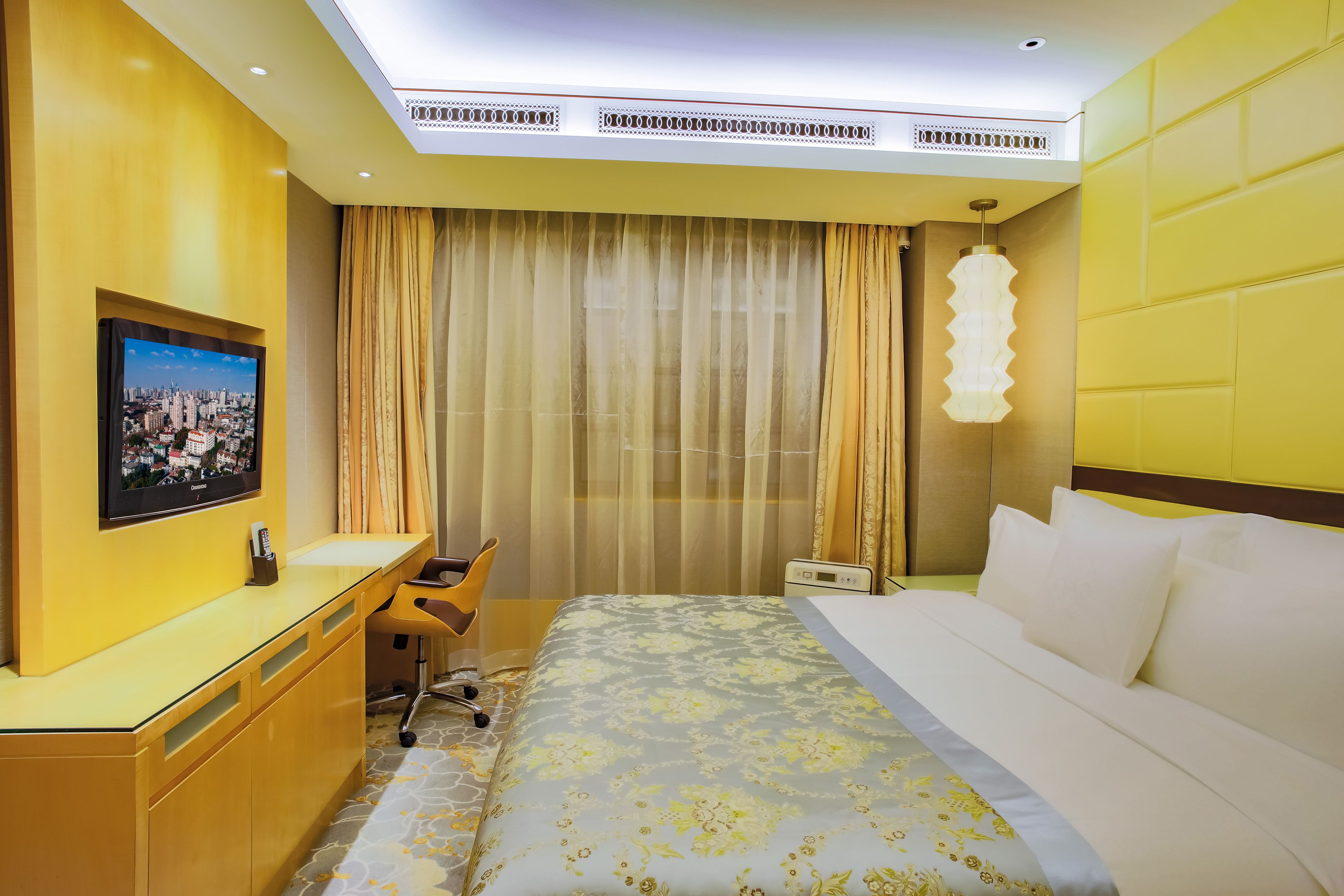 Ein Hotelzimmer mit Bett, Schreibtisch, Stuhl, Fernseher und einem Fenster mit Vorhängen.