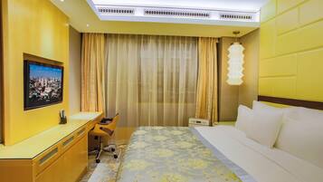 Ein Hotelzimmer mit Bett, Schreibtisch, Stuhl, Fernseher und einem Fenster mit Vorhängen.