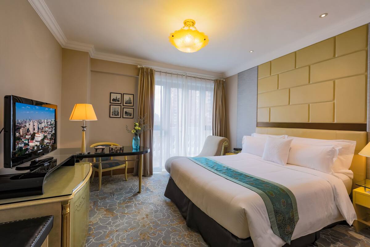 Hotellihuone, jossa on suuri sänky, työpöytä, jossa on televisio, tuoli ja lamppu.