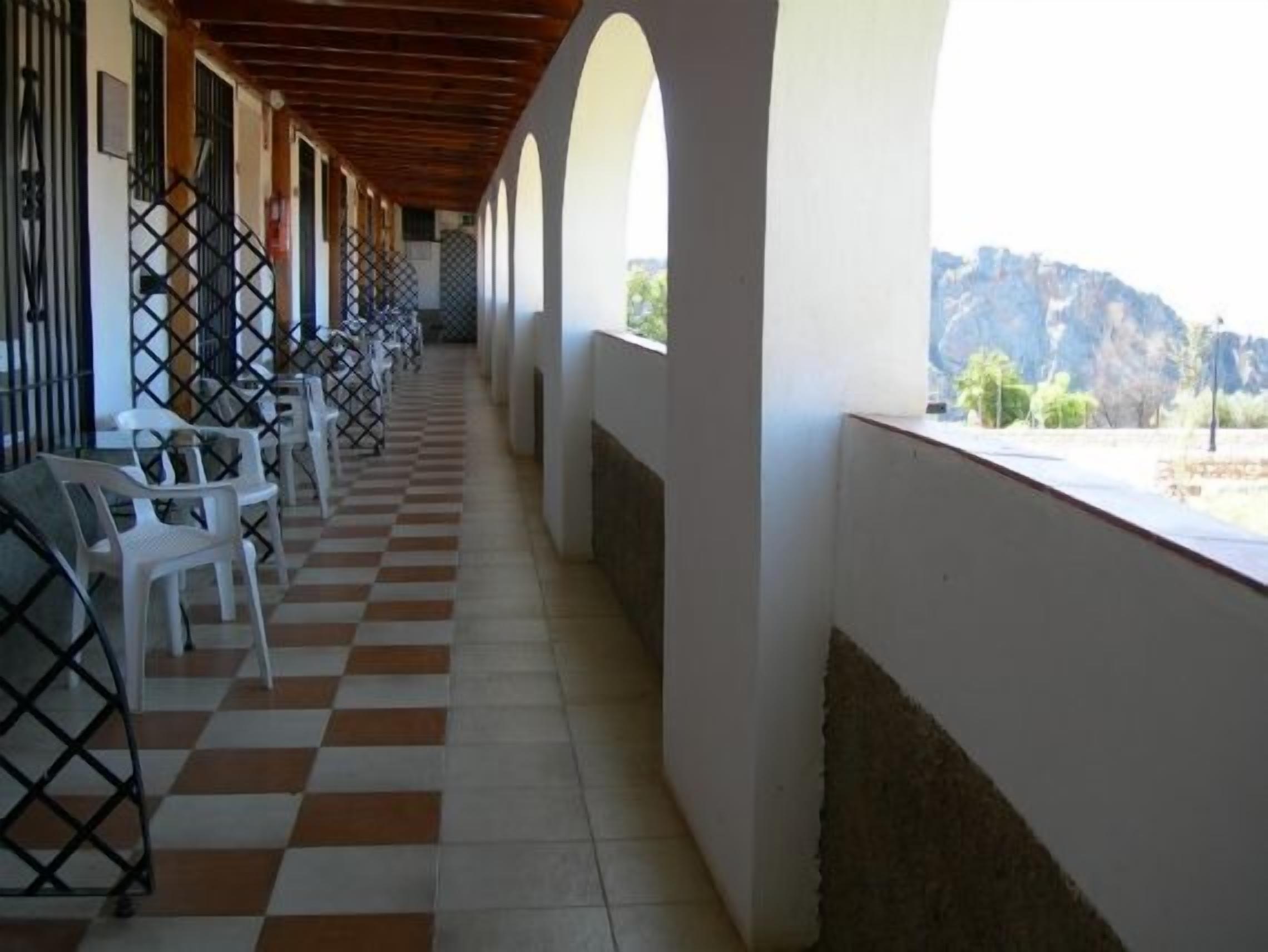 Un pasillo con piso a cuadros, paredes blancas y vista a un paisaje montañoso a través de amplias ventanas.