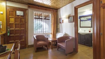 Een gezellige kamer met houten meubels, een eettafel, twee stoelen, een klein tafeltje en uitzicht buiten door een raam met tralies.