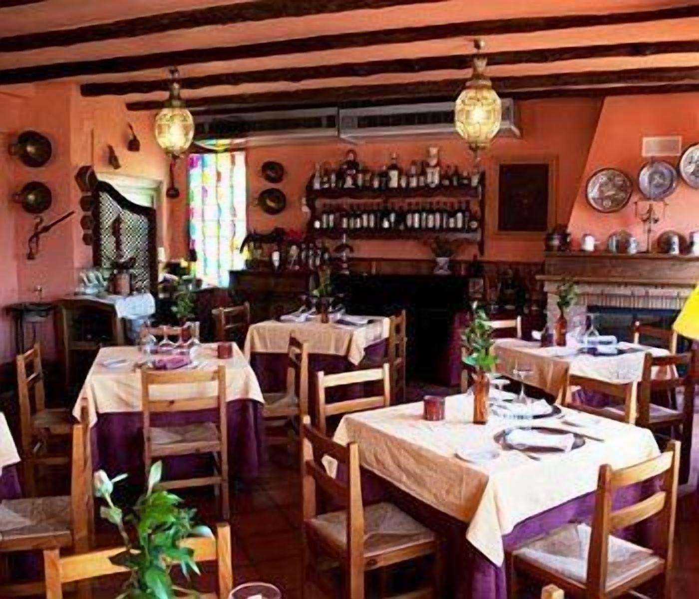 A cozy restaurant with wooden tables and chairs, a bar area with bottles, and a fireplace.