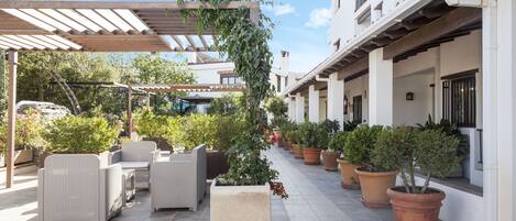 Un patio al aire libre con mobiliario de mimbre, plantas en macetas y una estructura de pérgola.