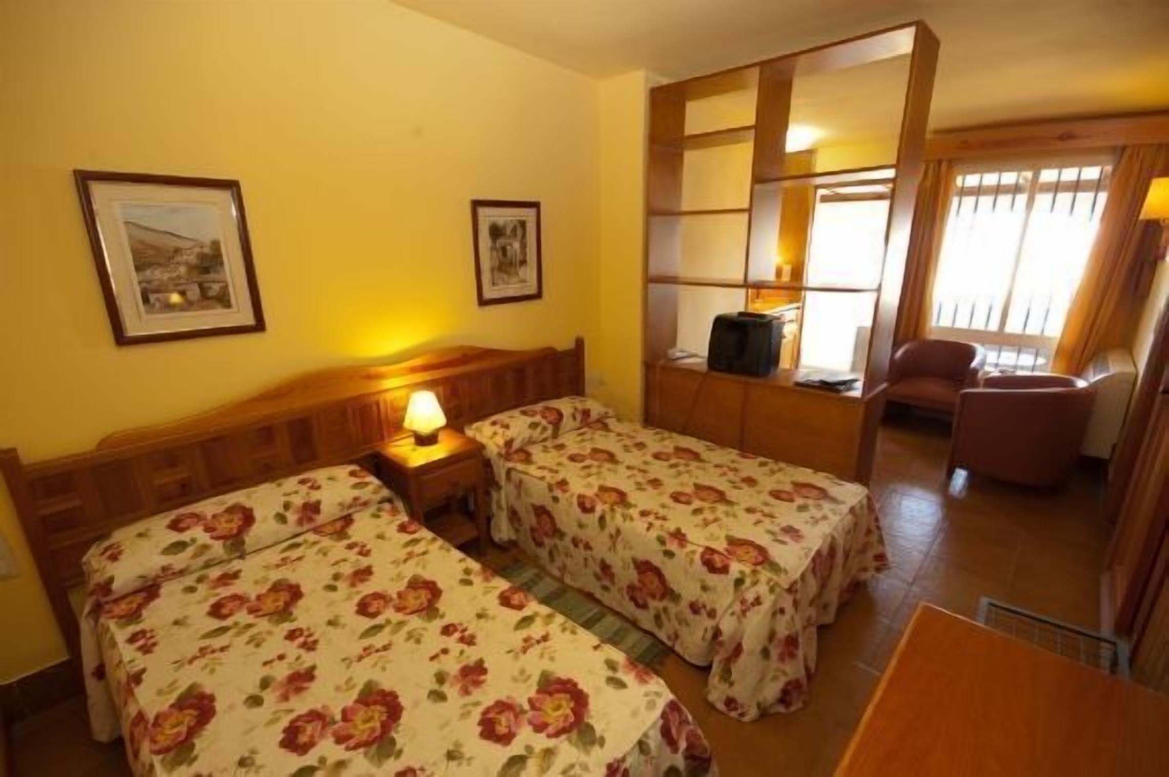 A room with two single beds, a wooden headboard, a small table, and a chair.