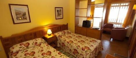 A room with two single beds, a wooden headboard, a small table, and a chair.